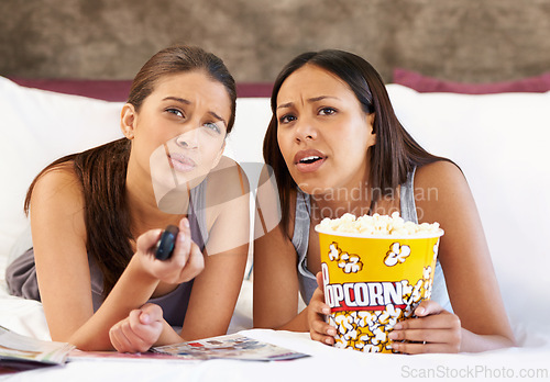 Image of Television, remote control and confused women on a bed with popcorn, movie or film in their home together. Watching tv, face and friends in a bedroom with theatre snack for Netflix, video or show