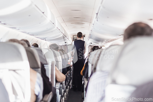 Image of Interior of airplane with passengers on seats and stewardess in uniform walking the aisle, serving people. Commercial economy flight service concept.