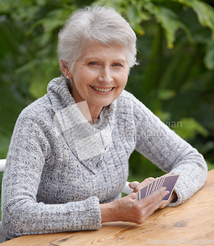 Image of Senior woman, portrait and outdoors playing cards, happy and game of bridge at park, garden or backyard. Elderly female, smile and poker at table for retirement fun on patio, porch or nursing home