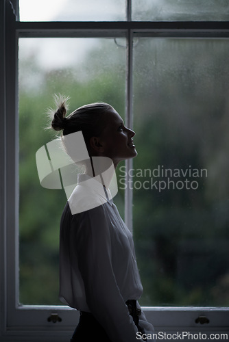 Image of Woman, profile and window for in home, dark room and mysterious aesthetic for hopeful or artistic pose. Female artist, dim light and dream or thinking, weather and night setting in overcast at house