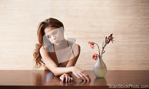 Image of Underwear, woman and sad with bra, flower and thinking at a table in a home with lingerie. Memory, morning and female person with mental health and nostalgia in a house with a plant and vase