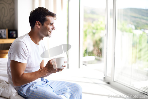 Image of Man, coffee and bedroom for happiness, smile and cup by window in house at holiday resort. Male person, happy and bed in pajamas or sleepwear for relaxation with tea or latte with drink at home.