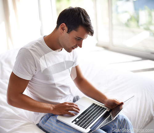 Image of Man, bed and laptop for communication, internet and technology in bedroom, home and apartment in morning time. Male person, student and computer on social media, browsing and online connectivity