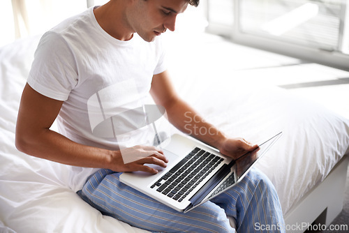 Image of Man, happy and laptop in bedroom, scroll and entertainment in pajamas and morning routine. Male person, browse and social media with technology, bed and smile in sleepwear at home for relaxation