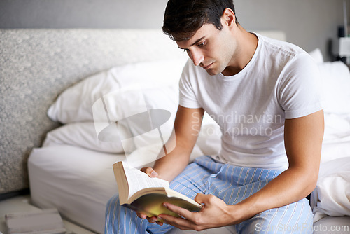 Image of Man, reading and pajamas for morning, routine and book in bedroom for wellness and literature for class. Male person, hobby and student for relaxation, leisure and novel for home free time in house