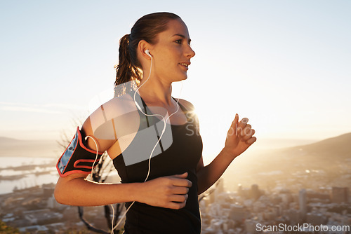 Image of Woman, running and sunset with earphones for workout, exercise or cardio training on mountain. Active female person or runner listening to music, podcast or audio for energy, health and wellness