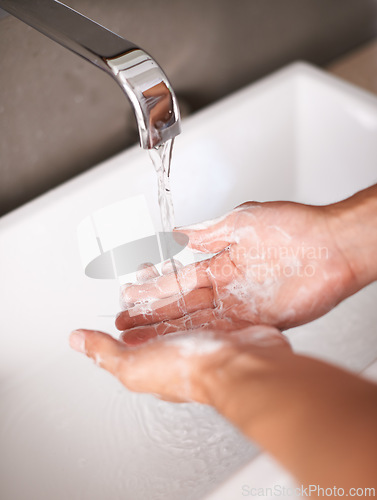 Image of Person, hands and soap with water for hygiene, cleaning or germ and bacteria removal in bathroom at home. Closeup of tap or faucet for disinfection, washing or rinsing in cleanliness by sink at house