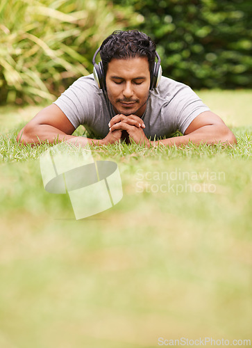 Image of Music, relax and man on grass in park, streaming sound on headphones for peace or wellness. Nature, audio or radio and happy young person lying on ground for break, rest or sleep in summer with space