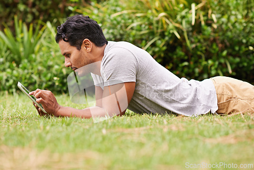 Image of Man, outside and tablet on grass, browse and watching social media or memes for entertainment in nature. Male person, backyard and tech to relax, scroll and vacation at home or house for peace