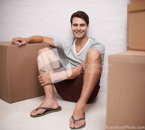 Image of Man, portrait and boxes on floor for moving with investment in real estate, new house and relax with happiness. Person, face and smile with cardboard on ground for storage, cargo and package in home