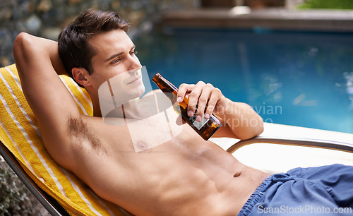 Image of Man, bed and drink by swimming pool with beer to relax or chill on summer vacation, luxury and resort or villa. Male person, bottle and alcohol for refreshments on tropical holiday in Maldives.