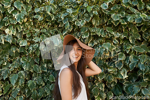 Image of Woman, portrait and happiness by hedge outdoor with travel, summer holiday and casual fashion with hat. Girl, face and smile at leaf fence in garden for relax, wellness and confidence in Amsterdam