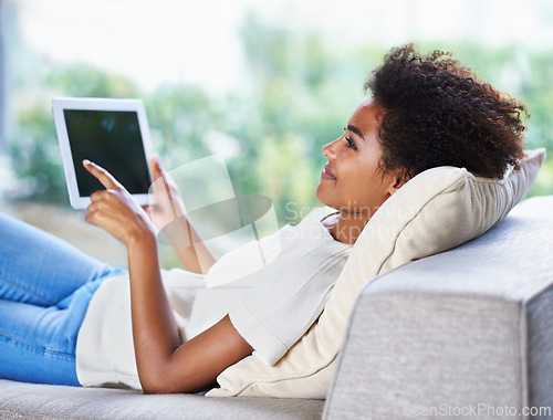 Image of Tablet, smile and relax woman on sofa, lying down and resting in home living room. Technology, touch screen and happy African woman with afro, couch and social media online for internet communication