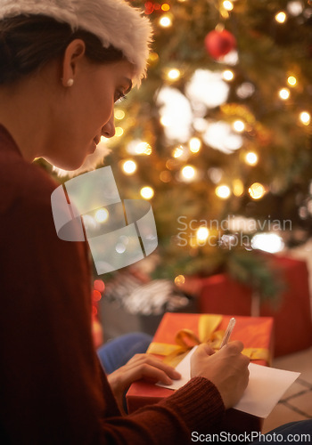 Image of Woman, writing letter and Christmas in home by tree, present and santa hat with message for festive wish. Girl, person and paper with notes, gift and package with kindness, celebration and xmas card