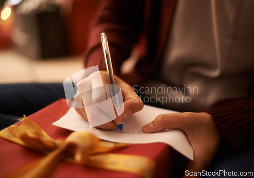 Image of Hands, writing letter and Christmas in home with box, present and message with festive wish in closeup. Person, pen and paper with notes, gift and package with kindness, celebration and xmas card