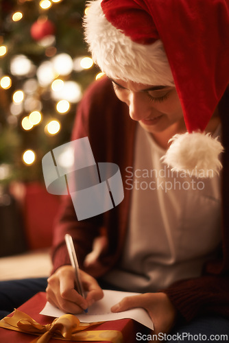 Image of Woman, writing letter and Christmas with smile by tree, present or santa hat with message for festive wish. Girl, person and paper with notes, gift or package with kindness, celebration and xmas card