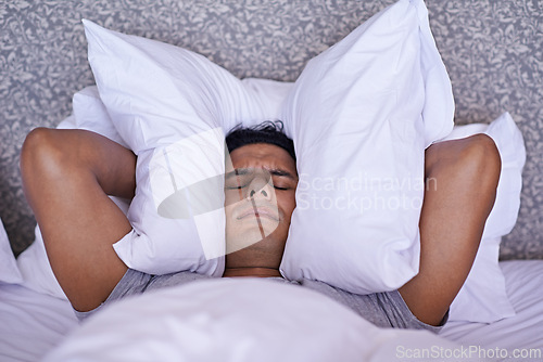 Image of Man, noise or insomnia in bedroom to rest, tired or cover ears with pillow for crisis of loud issue. Person, frustrated and mad for sound or sleep problem, anxiety and headache or stress in home