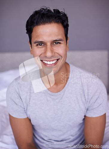 Image of Man, happy and wellness in bedroom in portrait, peace and confident on morning vacation on home. Young person, smile face and healthy on break on lazy weekend, pyjamas and rest on bed in apartment