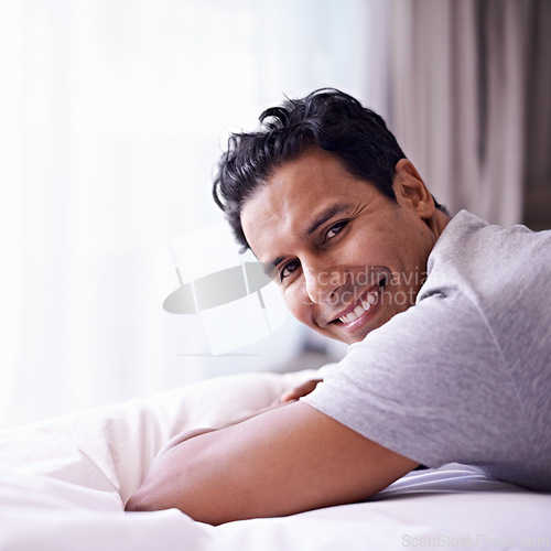 Image of Man, happy and calm in bedroom in portrait, wellness and confident person on morning in home. Young guy, positive face and healthy on break on lazy weekend, pyjamas and satisfied on bed in apartment