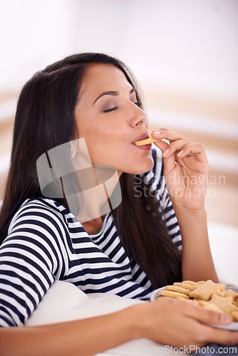 Image of Woman, cookies and eating in home on weekend, smile and satisfaction in living room for enjoyment. Female person, happy and snacks or biscuits for nutrition, relax and comfort food for wellness