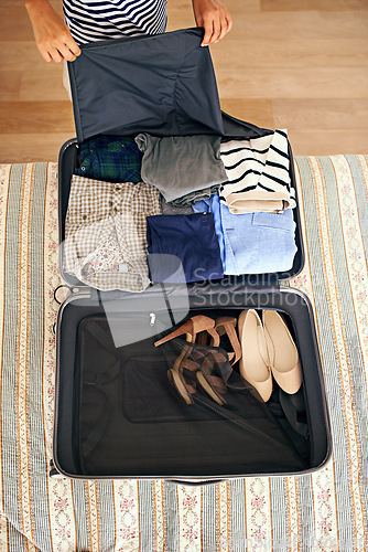 Image of Hands, travel and person packing suitcase in bedroom of home for holiday or vacation from above. Clothes, getting ready and luggage with tourist bag on bed of apartment, hotel or person for getaway