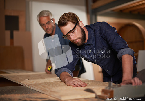 Image of Carpentry, team and man with wood saw for planning construction project or senior father teaching son. Machine, apprentice and mentor in woodwork, training and serious at workshop with plank on table