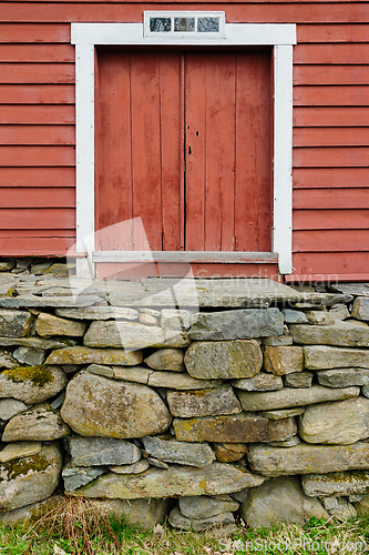 Image of Vintage red barn door perched on a rustic stone foundation amids