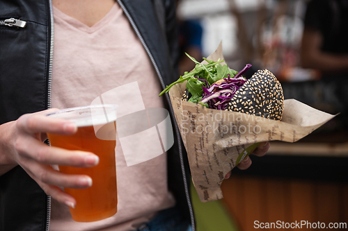 Image of Close up of woman hands holding delicious organic salmon vegetarian burger and homebrewed IPA beer on open air beer an burger urban street food festival in Ljubljana, Slovenia.