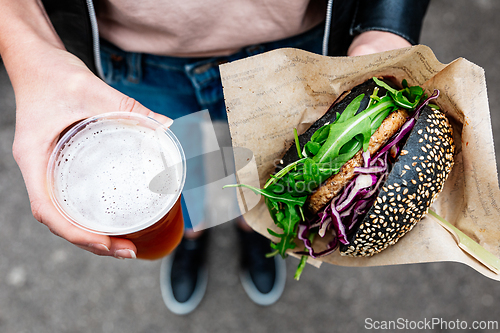 Image of Close up of woman hands holding delicious organic salmon vegetarian burger and homebrewed IPA beer on open air beer an burger urban street food festival in Ljubljana, Slovenia.