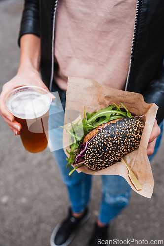 Image of Close up of woman hands holding delicious organic salmon vegetarian burger and homebrewed IPA beer on open air beer an burger urban street food festival in Ljubljana, Slovenia.