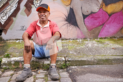 Image of Homeless, man and poverty in street, mature male person and graffiti art on wall in urban area. Smile, sitting and sidewalk in neighbourhood, third world or creative design in community for relax