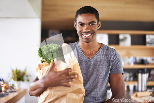 Image of African man, paper bag and groceries in home kitchen with smile for discount, deal and nutrition choice. Person, shopping and happy in apartment for product, sale and ready with portrait for cooking