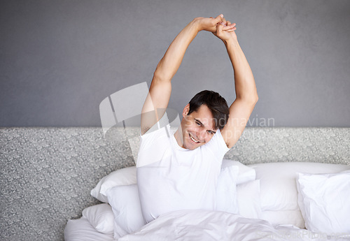 Image of Man, morning and smile in bed, house and stretching for daily routine and job for rest and wellness. Male person, happy and bedroom in pajamas, and home in awake and relaxing on Saturday day off