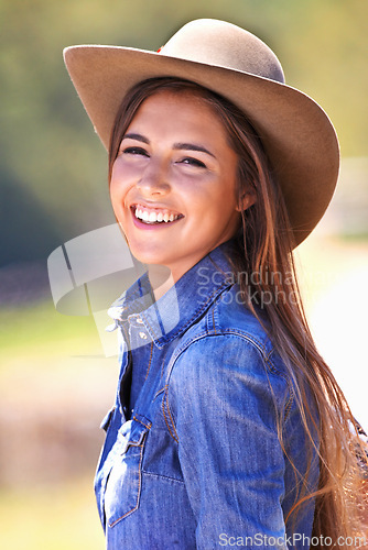 Image of Happy woman, portrait and cowgirl with hat on farmland for adventure, travel or outdoor journey in Texas. Female person with smile in western fashion, denim shirt and cap at ranch in the countryside