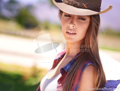 Image of Fashion, summer and cowgirl in hat on farm or ranch for agriculture or sustainability in countryside. Face, texas or western with young farmer leaning on fence in field organic or green farming