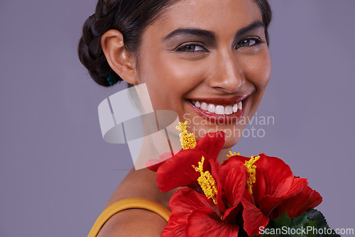 Image of Portrait, smile and woman with flowers for makeup, skincare or health isolated on a purple studio background in India. Face, person and cosmetics with bouquet for natural beauty with organic hibiscus