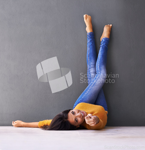 Image of Woman, smile and wall background for point, feet on wall and relaxing on floor in portrait with fashion. Female person, choice and chill at home for happiness, hey you and wellness in jeans with toes