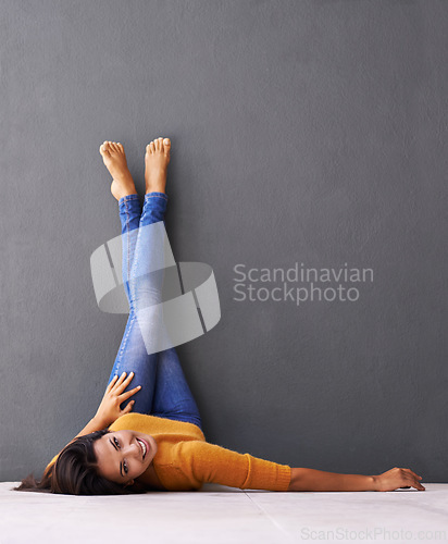 Image of Woman, smile and wall background, trendy, clothes on wall and relaxing on floor in portrait with fashion. Female person, happy and chill at home for happiness and wellness in jeans upside down