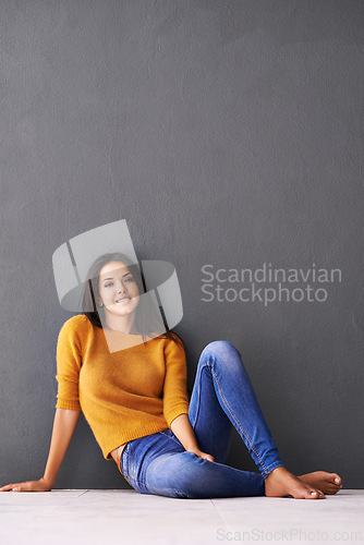Image of Portrait, girl and relax or chill on floor with casual outfit for fashion or comfort, leisure and wellness with smile. Female person, isolated with grey background or wall for clothing with mockup.