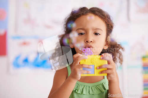 Image of Preschool, toy and girl playing with bubbles for growth and development of child with game. Kindergarten, soap and wand with cute kid for fun in classroom with drawings by youth in background