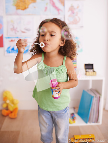 Image of Girl, toy and blowing bubbles for development, playing and having fun alone in room. Happiness, growth and face of young child in kindergarten for learning, soap bubble wand and activity games