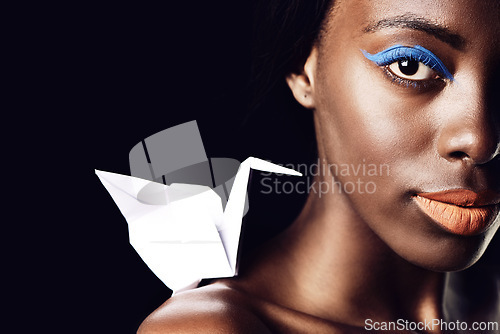 Image of Black woman, portrait and makeup with cosmetics, fine art and origami bird or dove on a dark studio background. Closeup or face of African female person or model with beauty eye color on mockup space
