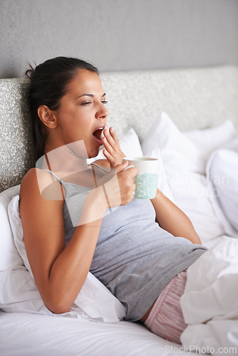 Image of Woman, bedroom and coffee in morning with yawn for waking up, tired and exhausted at home. Female person, relax and sleepy gesture with mug in apartment for day off, weekend and beverage on pillow