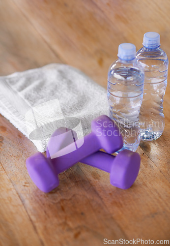 Image of Closeup, water bottles and towel with dumbbells, ground and exercise with equipment and nutrition. Weights, h2o and cloth with wooden floor or fitness with workout or training with wellness or health