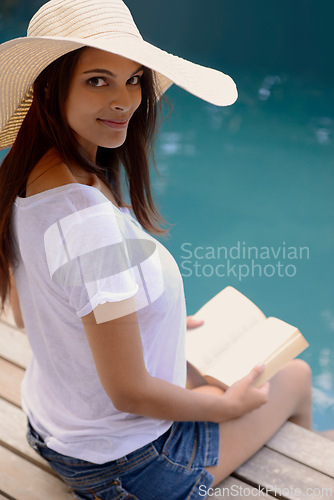 Image of Holiday, portrait and woman at pool with book, hat and relax with happy summer travel on hotel patio. Vacation, deck and girl with smile, reading and story with sunshine, weekend and luxury resort