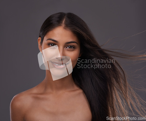 Image of Hair care, wind and portrait of happy woman with beauty, shine and skincare isolated on a gray studio background. Hairstyle, cosmetics and face of Indian model in salon with makeup at hairdresser