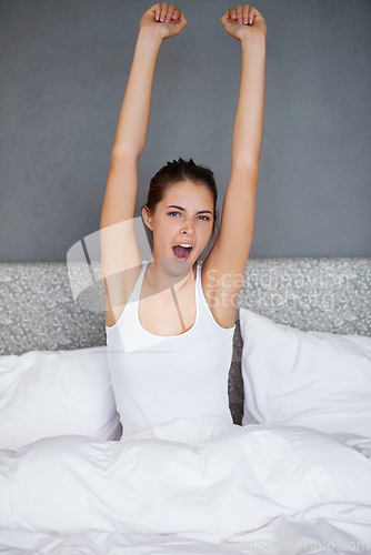 Image of Woman, stretching and portrait in bed with yawn in morning and wake up with fatigue after resting. Tired, girl and sitting in bedroom with exhausted energy and relax on holiday or vacation in home