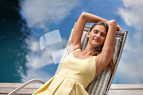 Image of Pool, fashion and woman relax on chair in summer, holiday or calm vacation in California. Girl, smile or sitting outdoor on deck in backyard or garden with peace at water with casual style in clothes