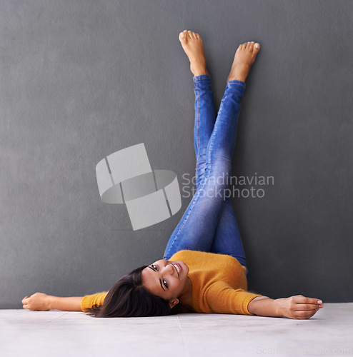 Image of Portrait, woman and smile to relax on floor with a dark wall background in casual style. Leisure, rest and face of female person with rest and fashion upside down with her feet on a studio backdrop