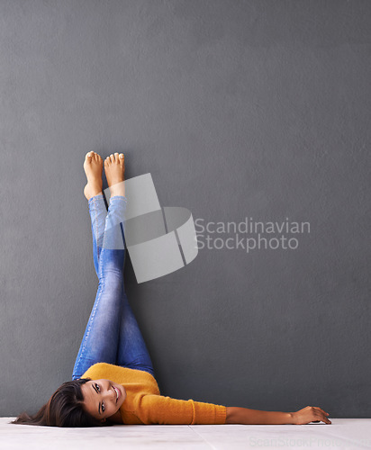 Image of Portrait, floor and happy woman relax with casual style on a grey wall background for rest. Leisure, style and face of smiling female person upside down on a dark studio backdrop for fashion